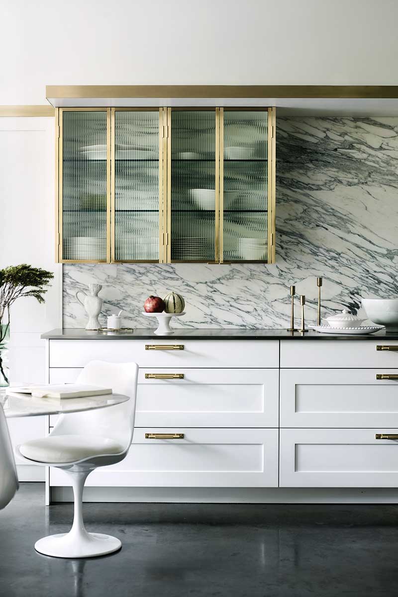 A white kitchen with a marble splashback and dark flooring 