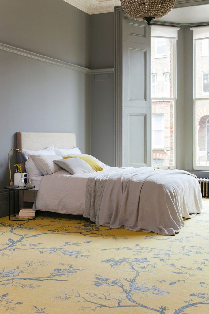 Room with grey walls, neutral bed, and bright yellow patterned carpet